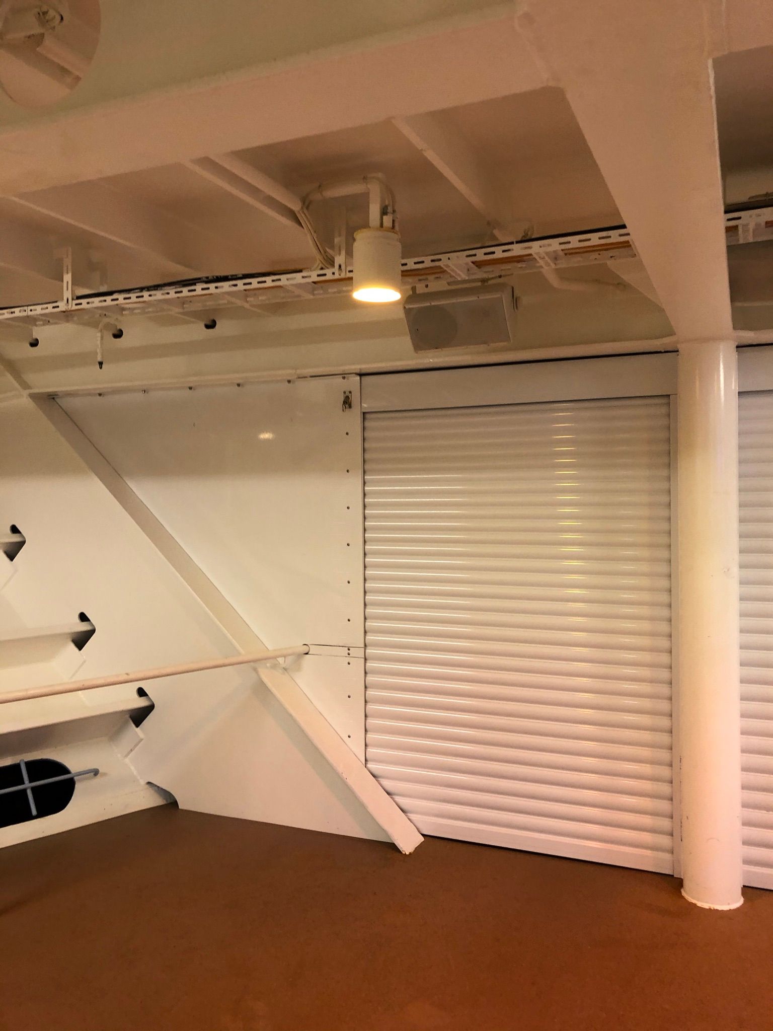 Loft interior with white beams, wall shelves, and a closed white rolling shutter door