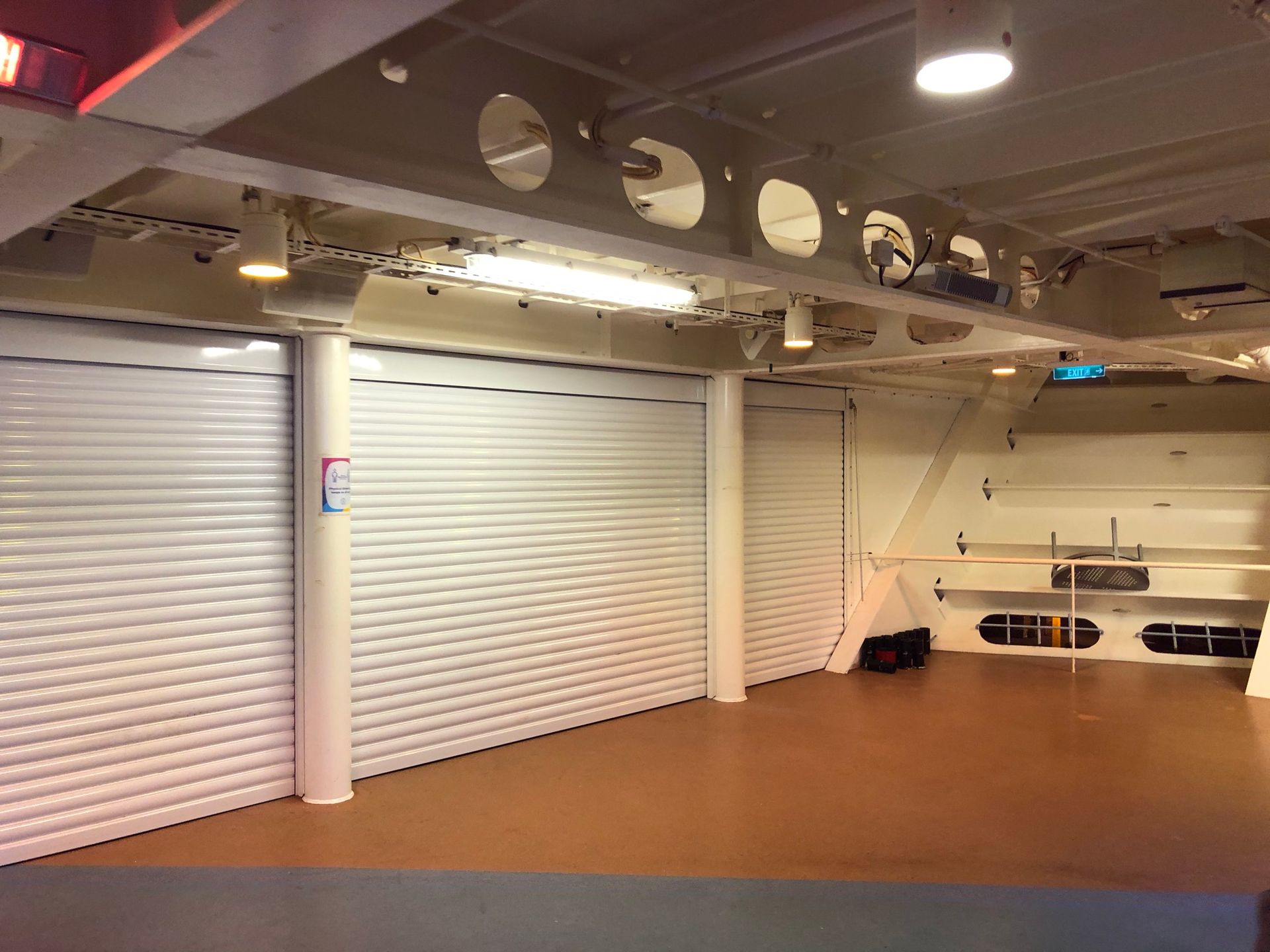 Empty indoor room with white roll-up shutters and brown floor under exposed ceiling lights