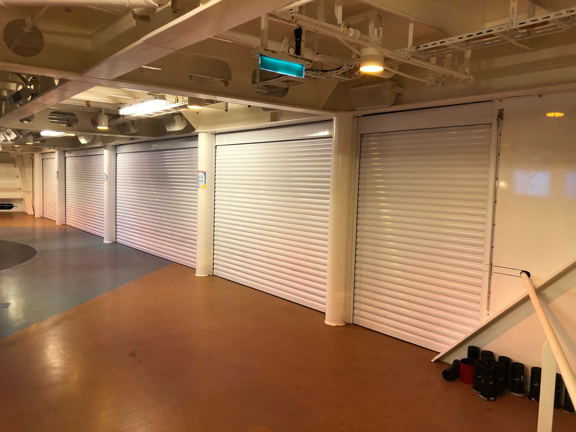 Empty industrial corridor with white roll-up doors and a brown floor under ceiling lights