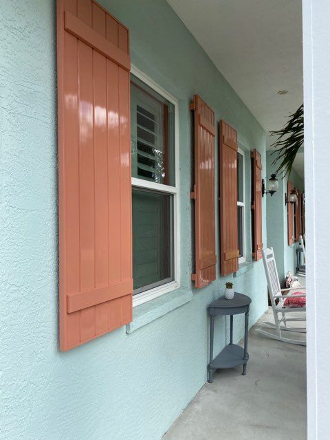 Pastel-blue house wall with orange shutters, windows, and a small lantern on a porch walkway