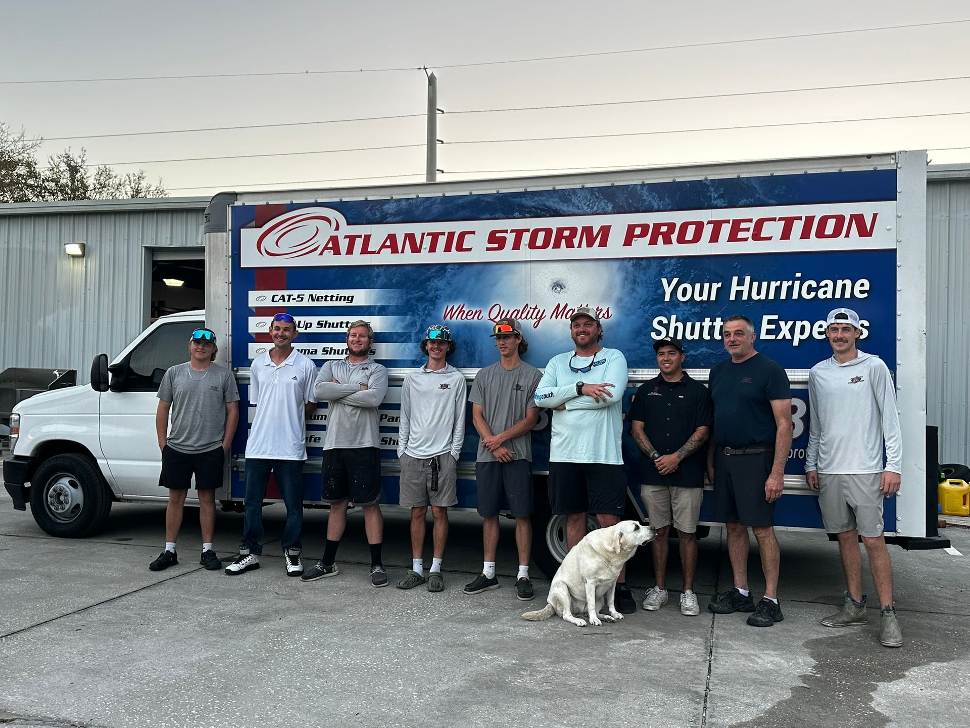 Storm protection team posing in front of a branded truck and trailer, with a dog in front.