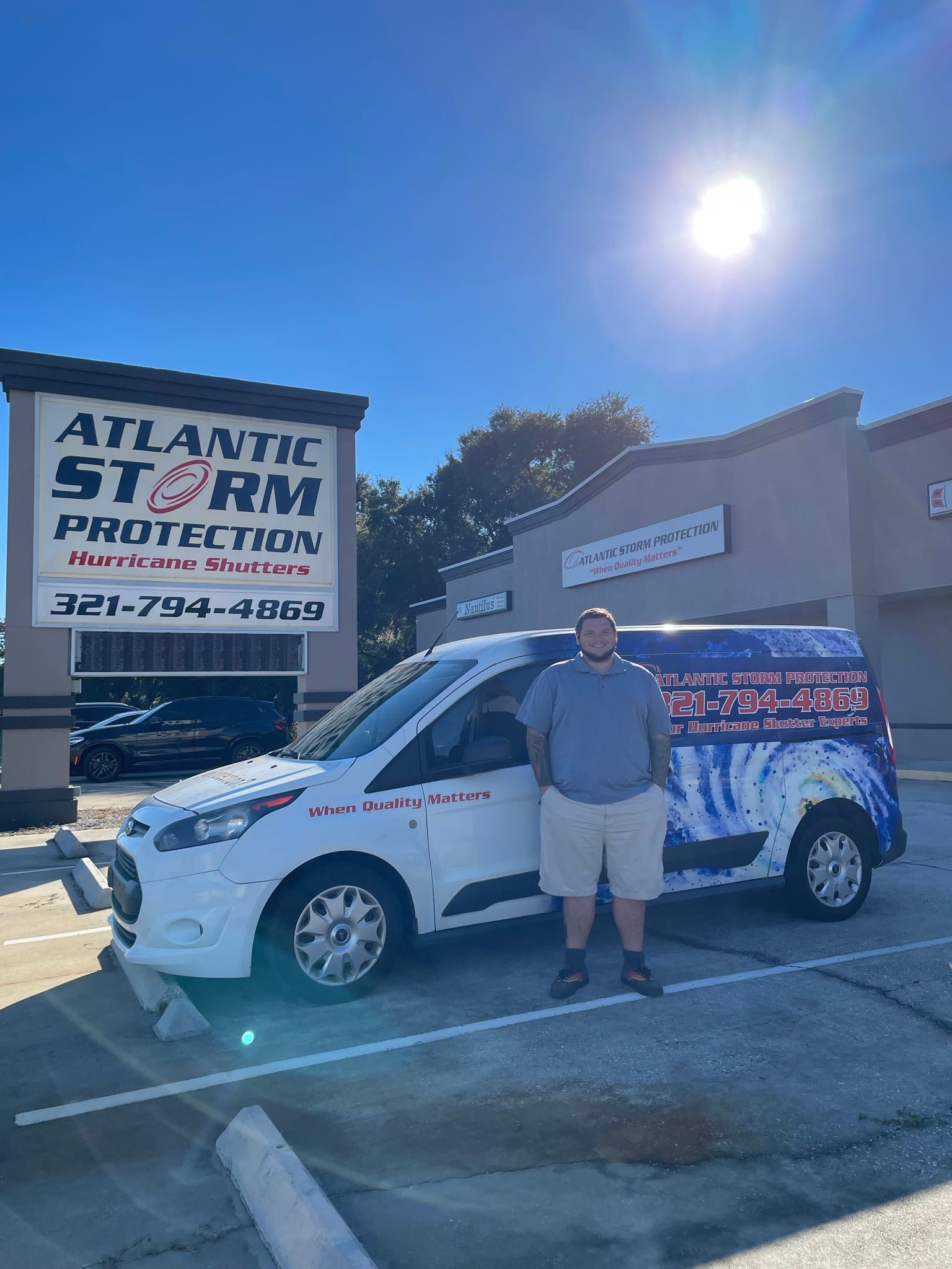 Man standing beside a white van with colorful graphics outside Atlantic Star Automotive under a bright sun