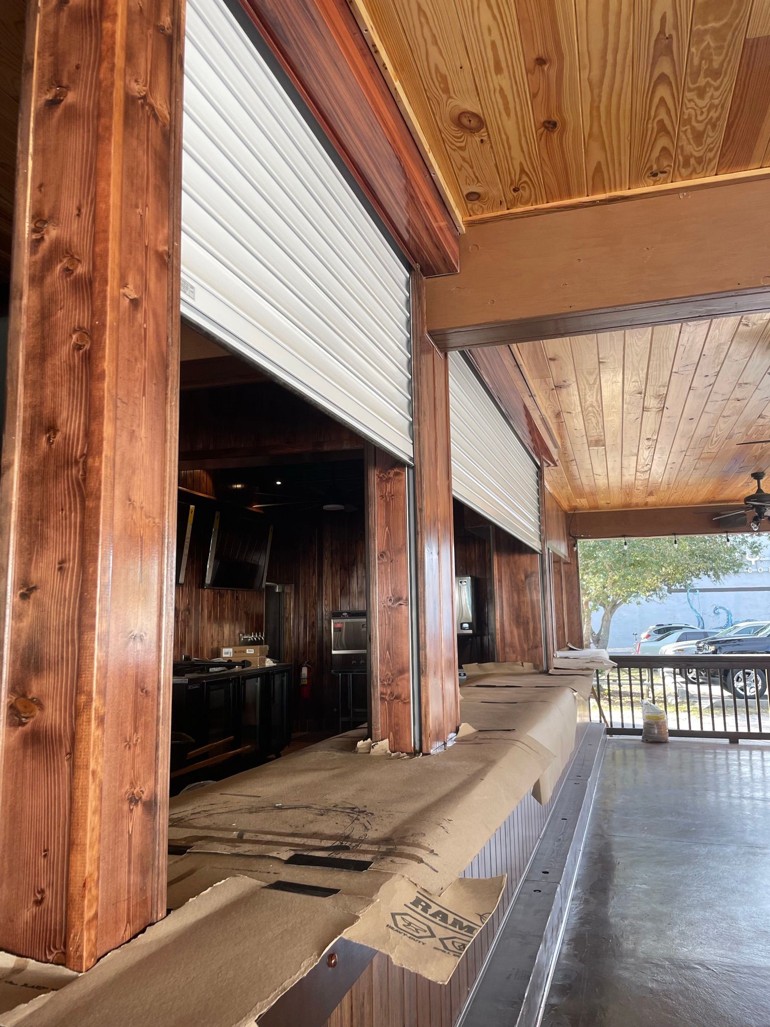 Open-air wooden patio with roll-up shutters, bar seating, and a view of the street beyond.