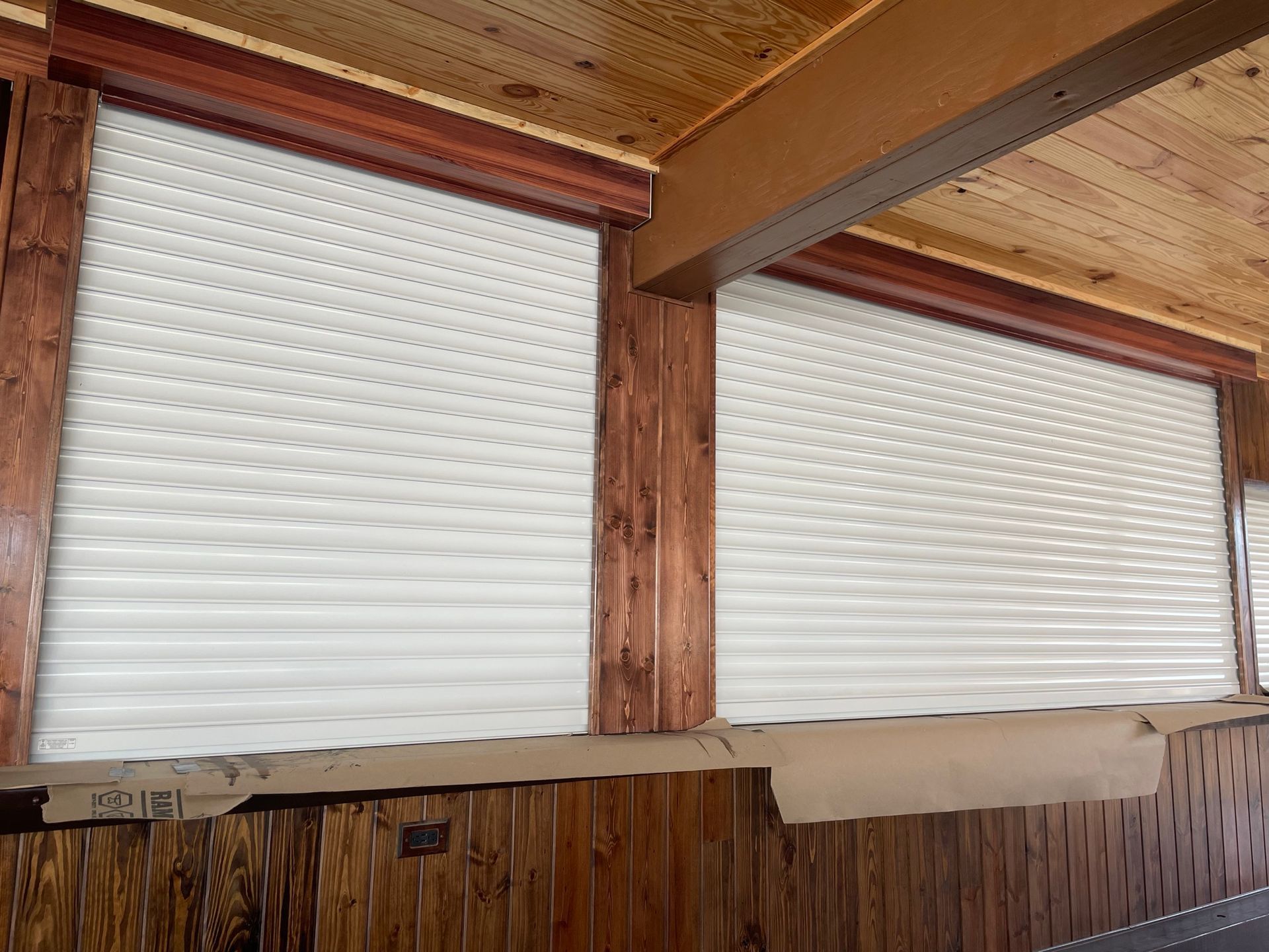 Two large white window blinds beneath a wooden porch ceiling and beams