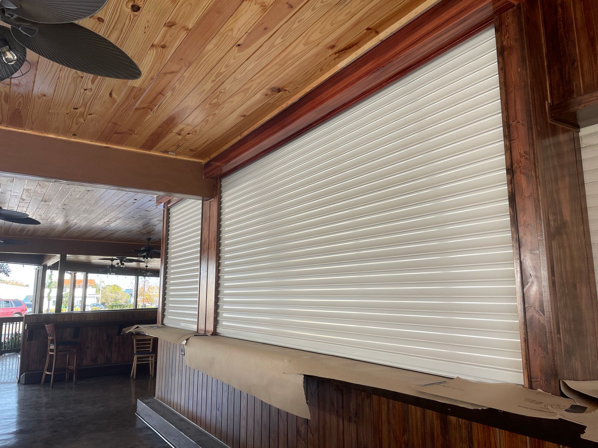 Closed white roll-up service window in a rustic wooden bar or patio area.