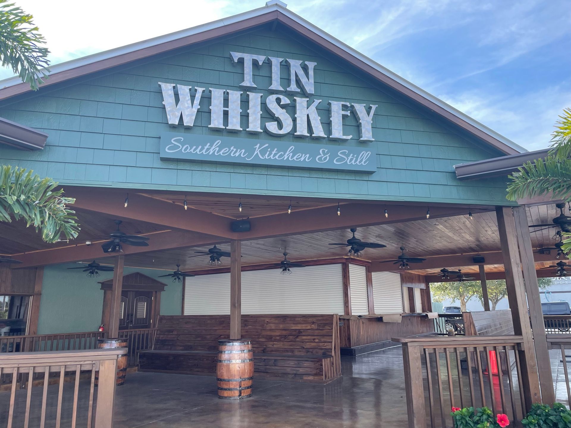 Tin Whiskey restaurant exterior with green sign, wooden porch, and barrel accents
