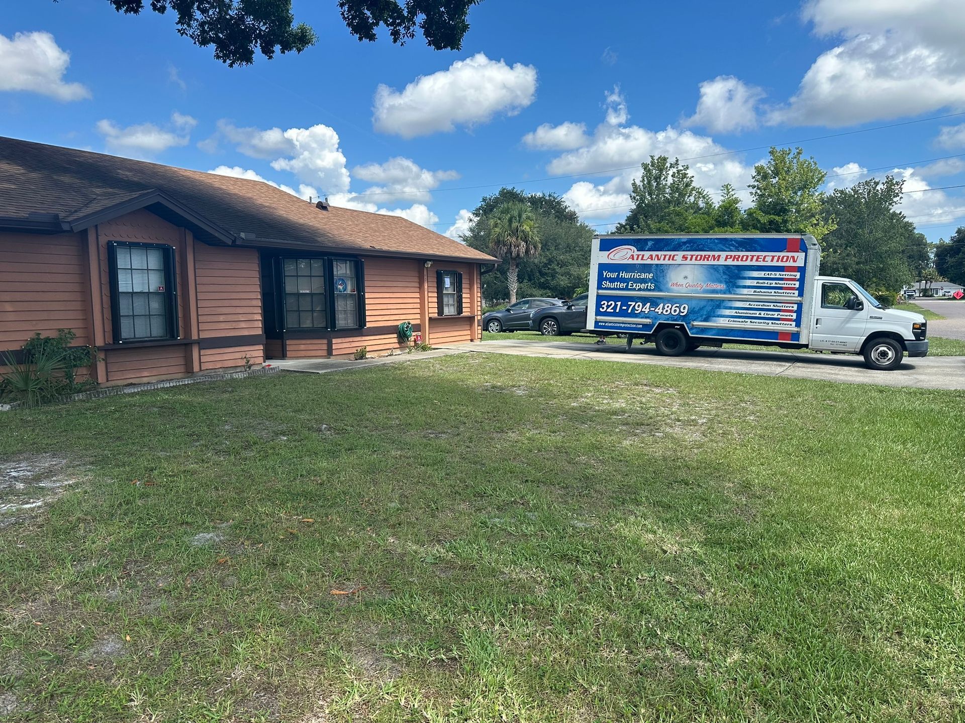 Single-story wooden house with a white service truck parked on a grassy yard under a blue sky