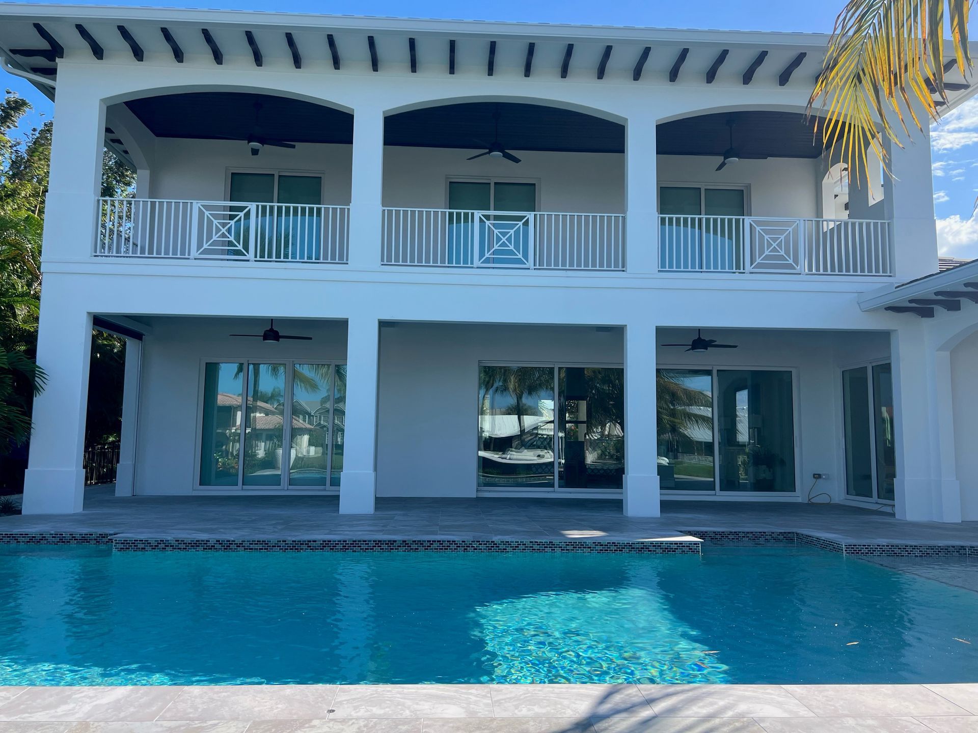 White two-story house with arched balconies and a backyard swimming pool under a blue sky