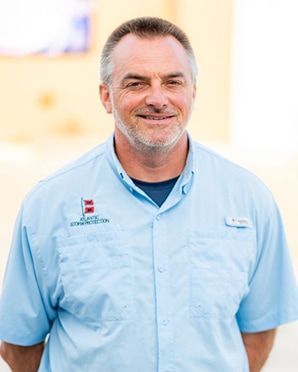 Smiling man in a light blue collared shirt standing outdoors against a blurred background