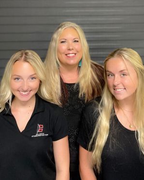 Three smiling people in black shirts posing against a gray backdrop