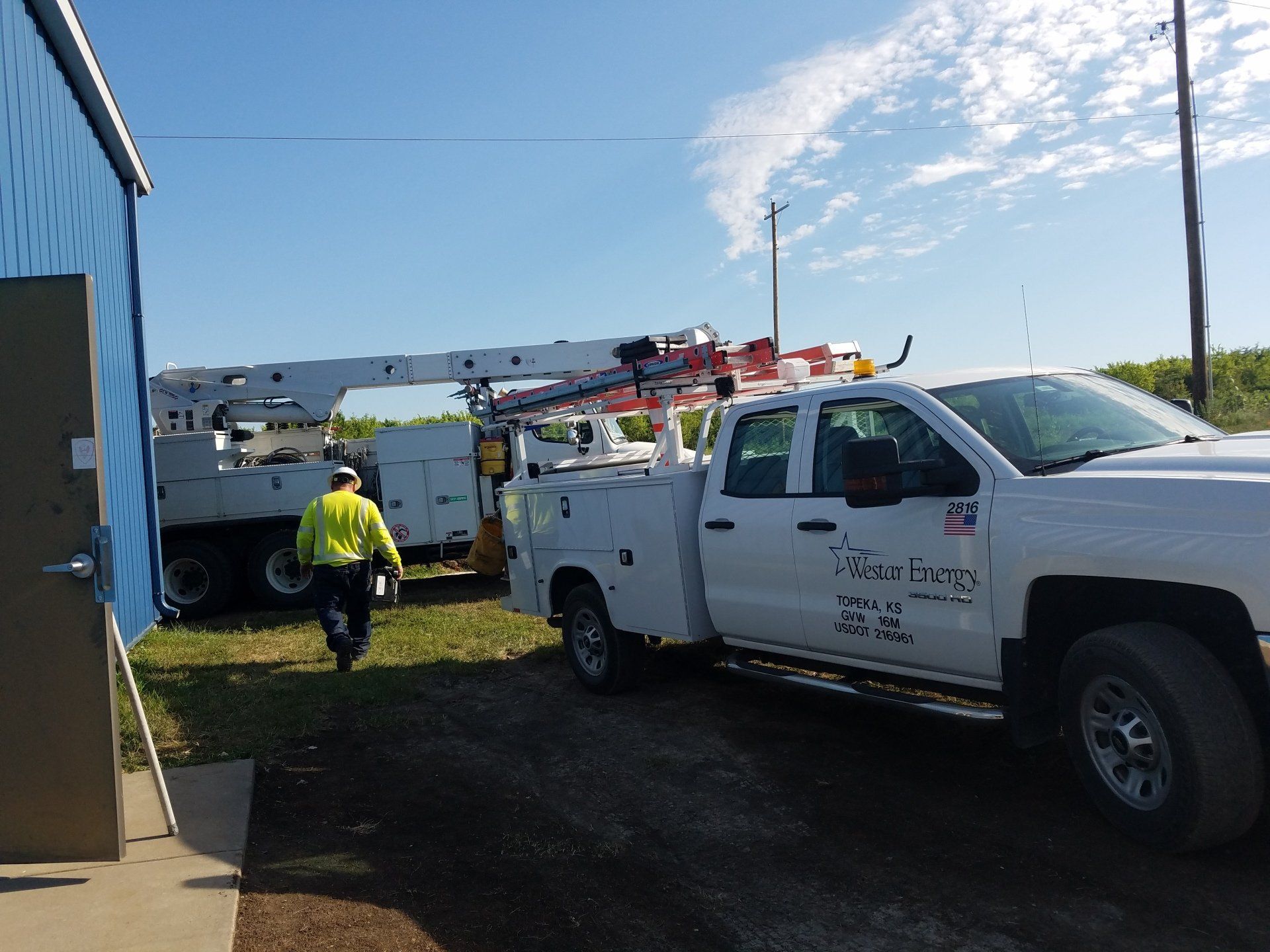 White utility truck next to a building, with a worker walking towards it under a partly cloudy sky.