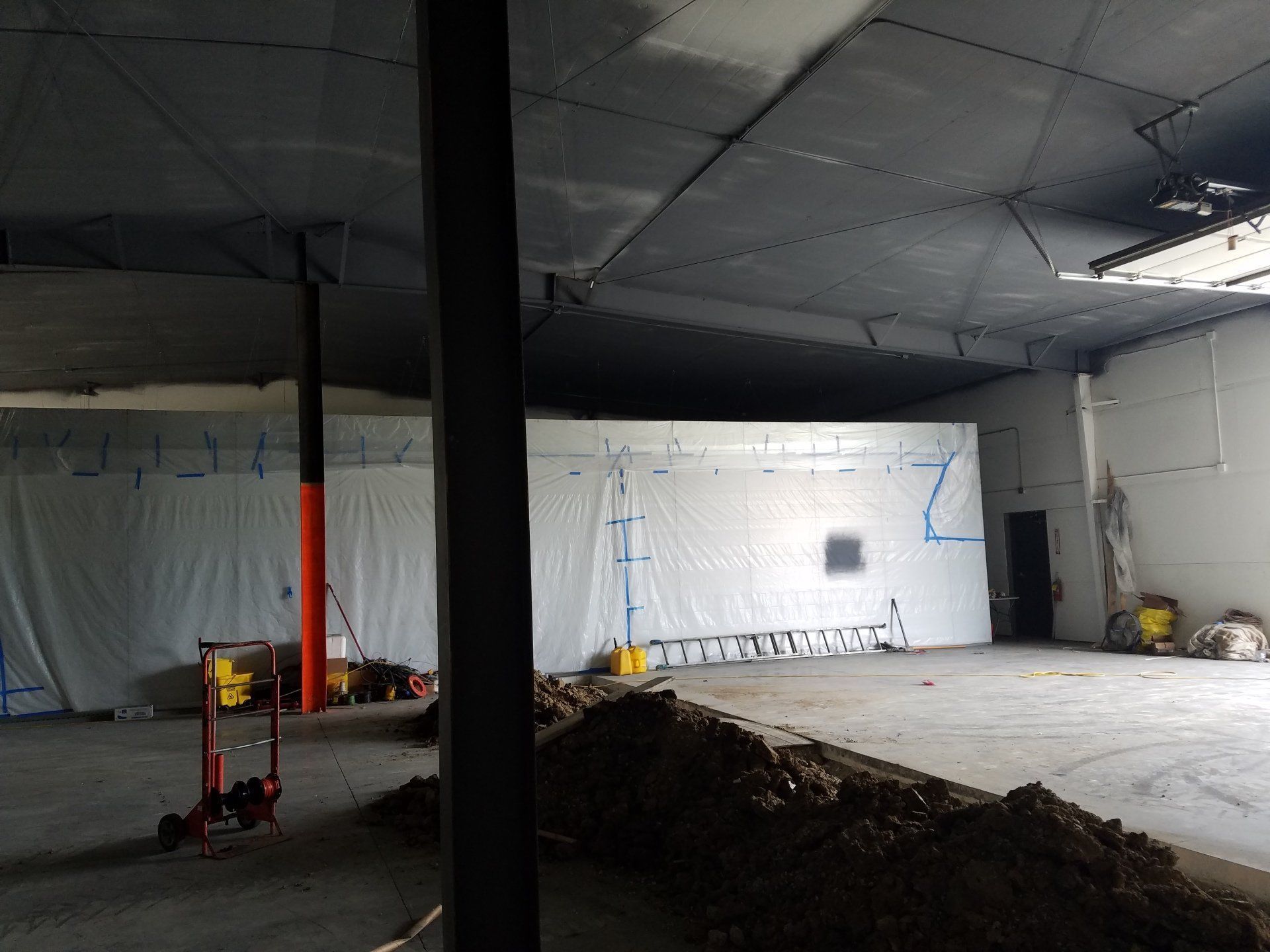 Interior of a construction site. Dark ceiling, white walls covered in protective sheeting, dirt pile on the floor.