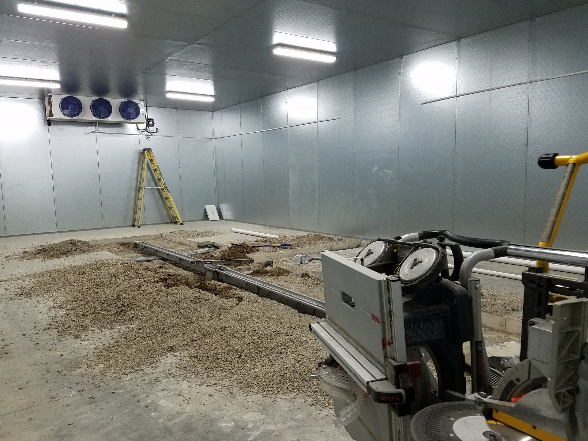 Interior of a refrigerated warehouse under construction, with cutting equipment and debris on the floor.