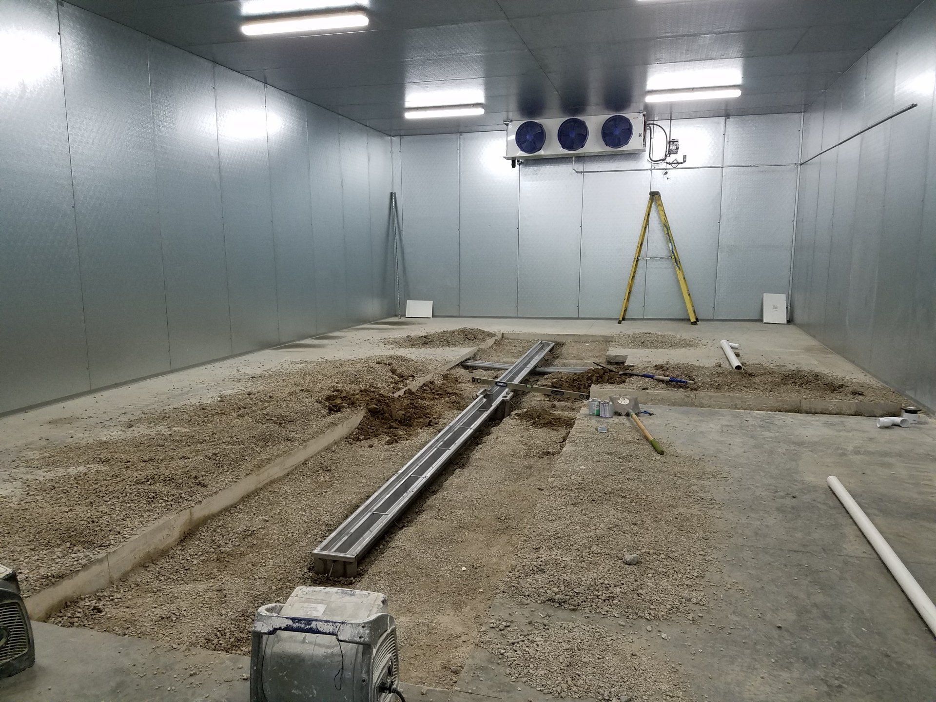 Interior of a large, cold storage room under construction with a gravel floor, metal walls, and HVAC unit.