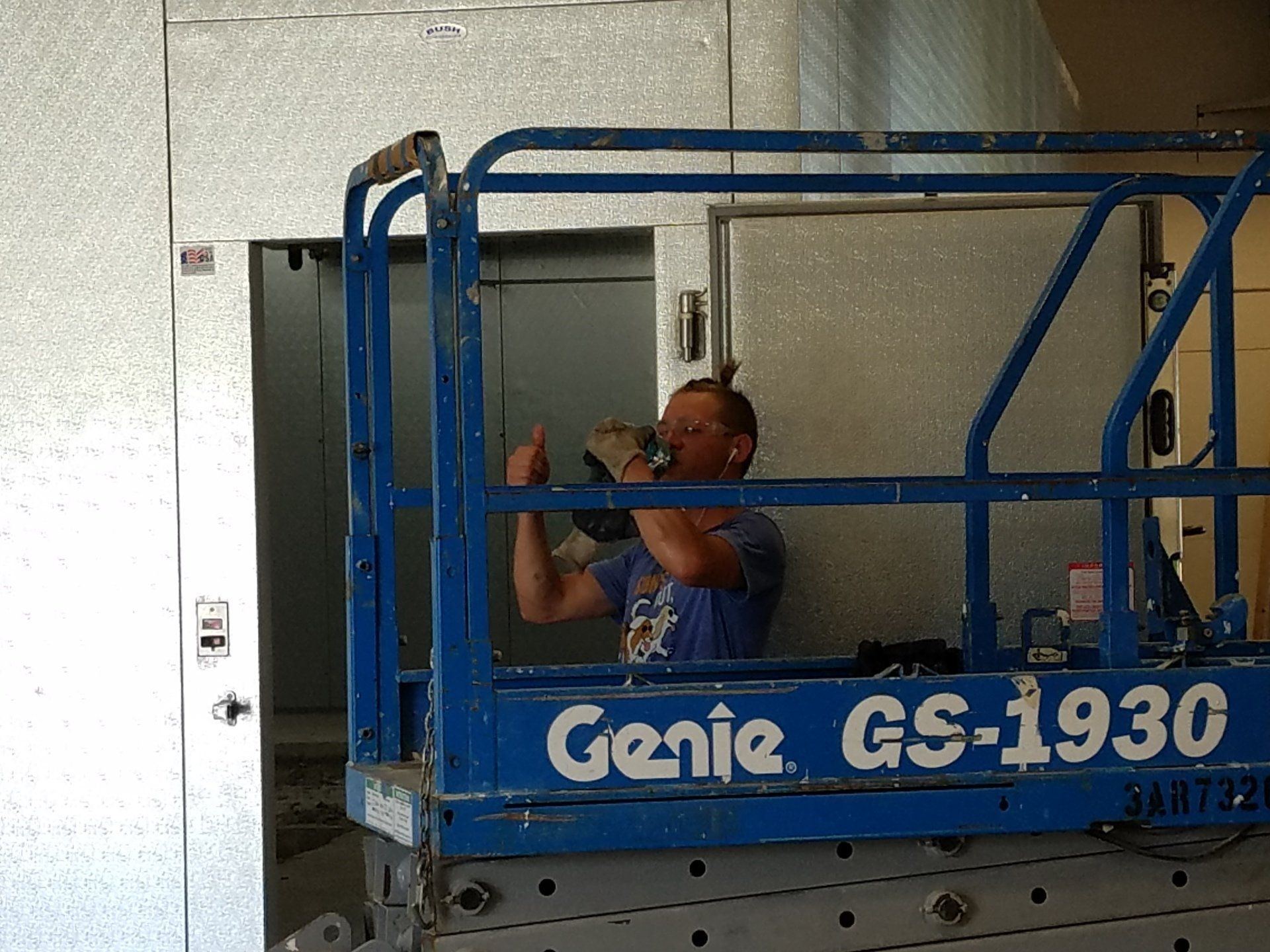 Man in lift, holding equipment, by an elevator door. The lift says