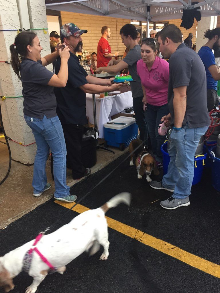 People and dogs at an outdoor event. Man holding item, others watching. Two dogs on leashes.