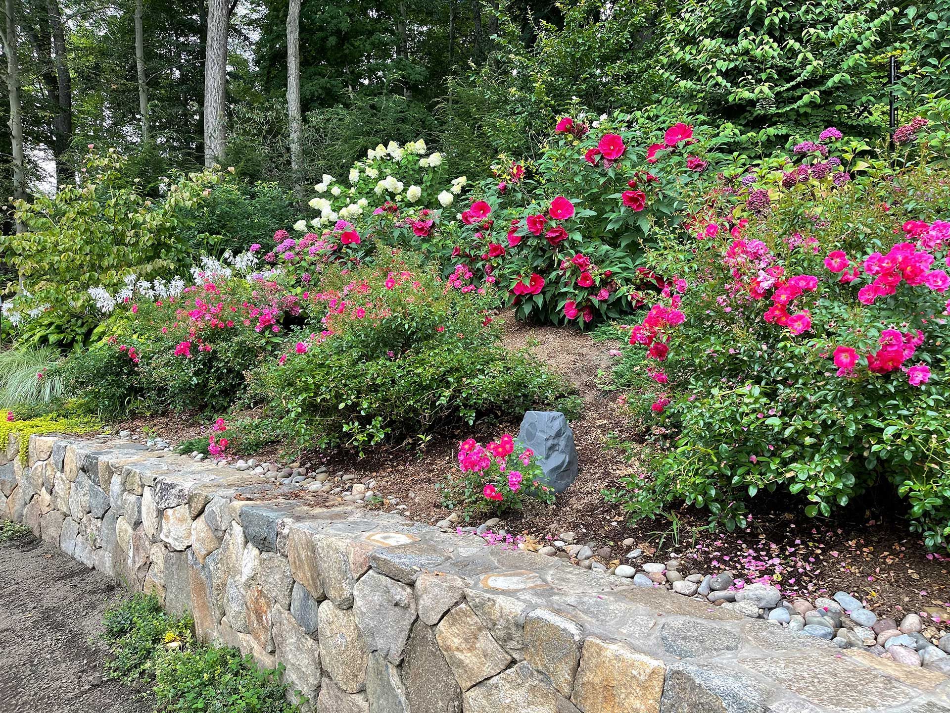 a stone wall surrounded by flowers and bushes in a garden