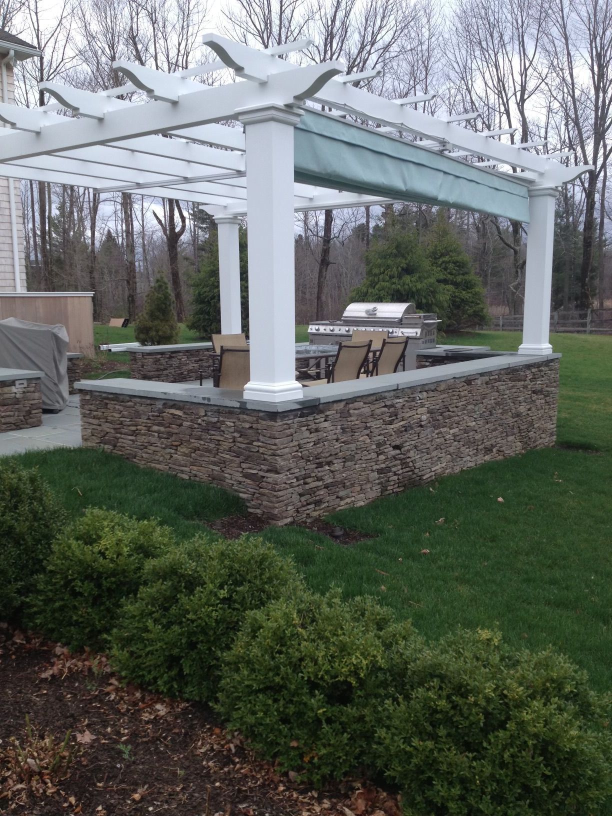a pergola with a grill underneath it in a backyard