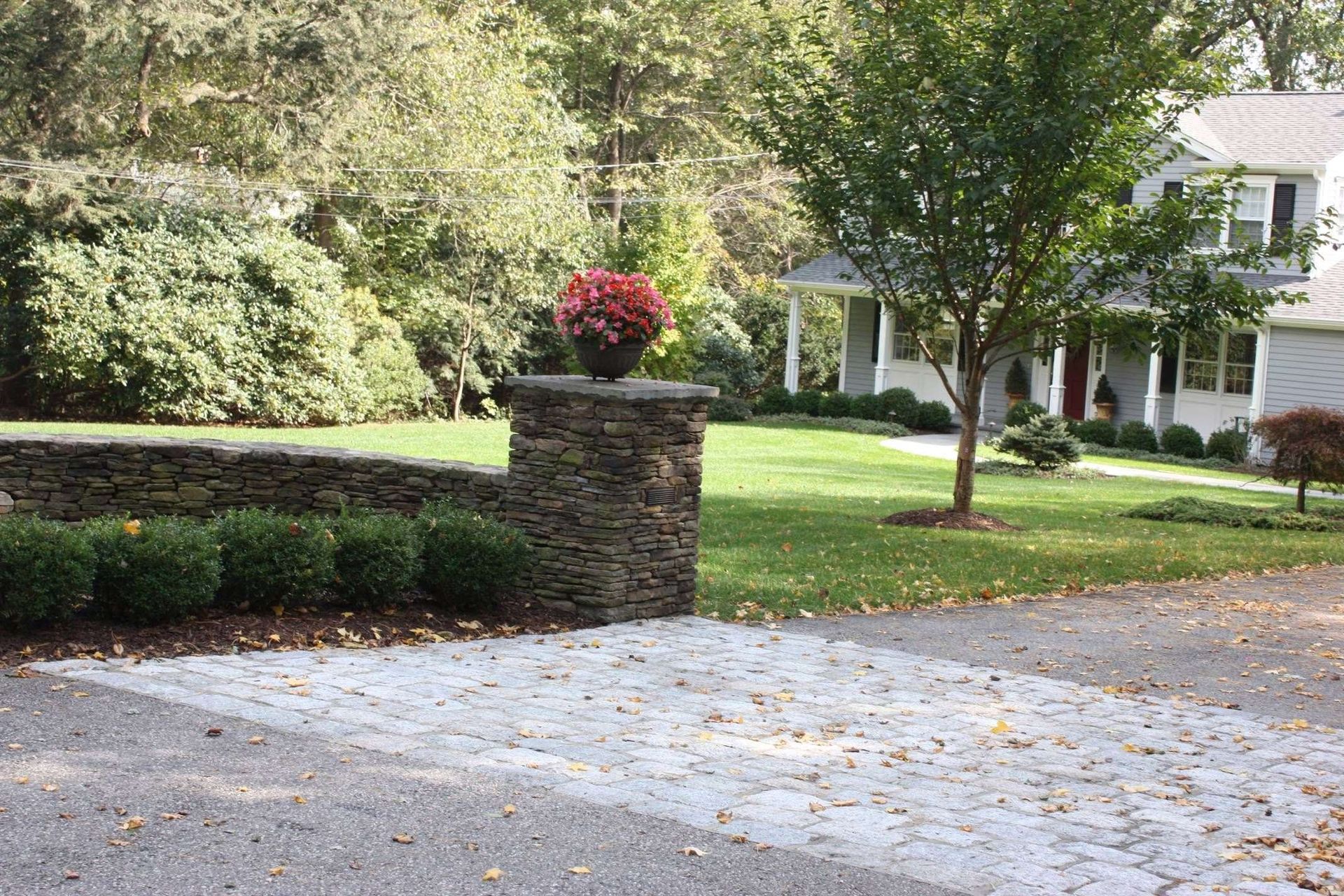 A driveway leading to a house with a stone wall