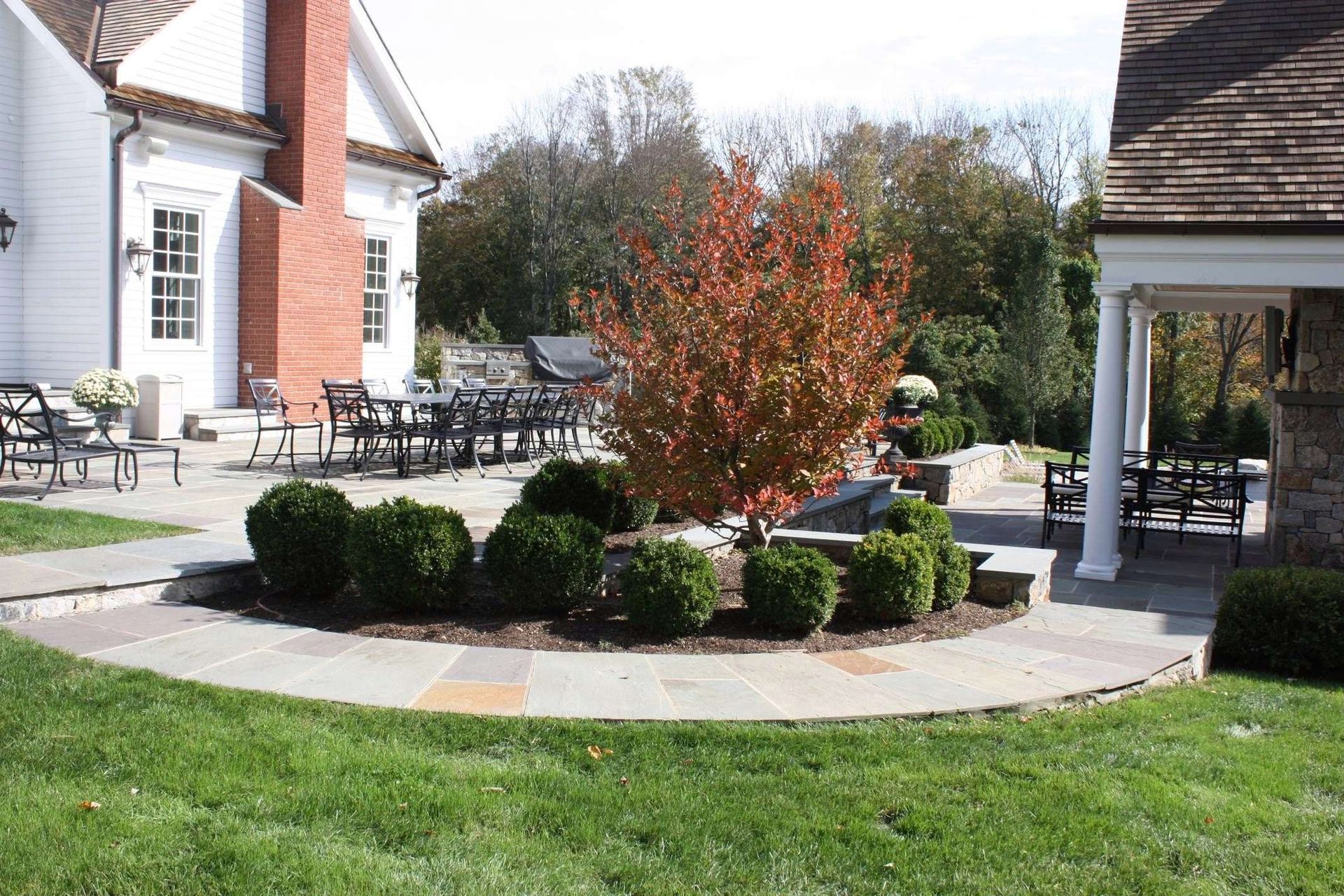 A white house with a brick chimney is surrounded by a lush green lawn