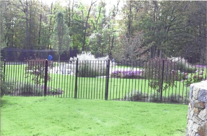 A wrought iron fence surrounds a lush green yard.