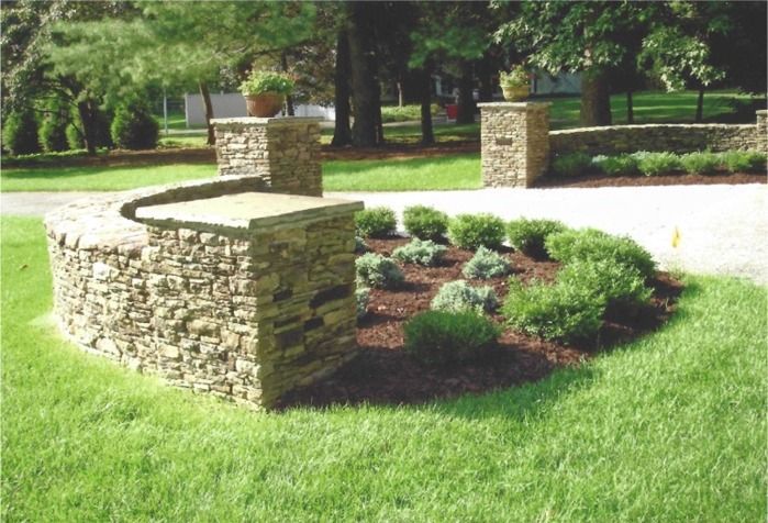 A stone wall is in the middle of a lush green yard