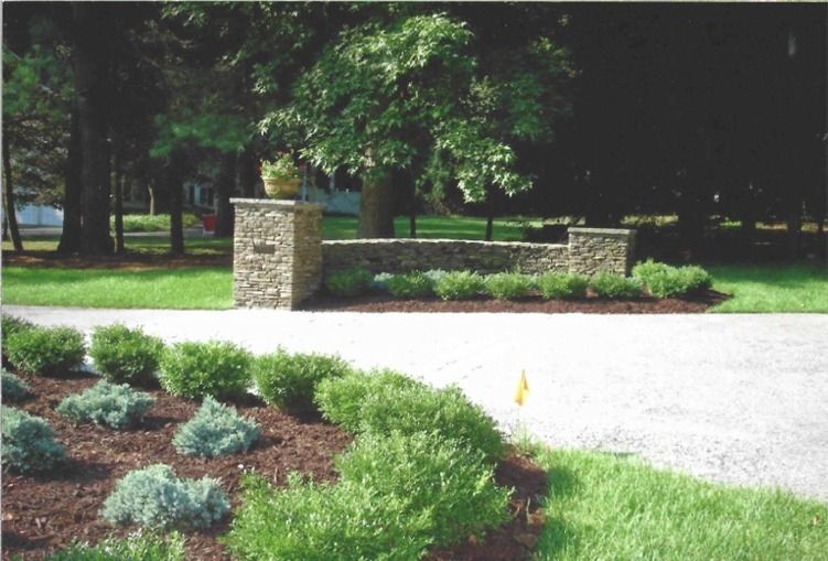 A driveway with a stone wall and bushes along the side