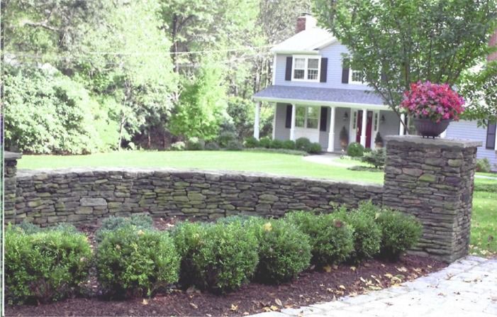 A house with a stone wall and bushes in front of it