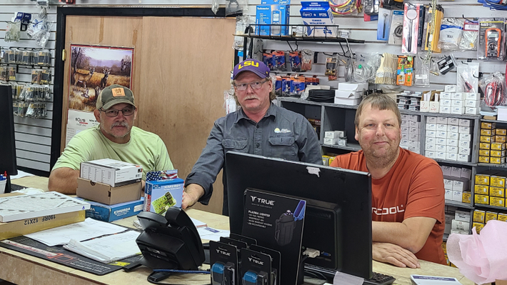 Three men are sitting at a desk in front of a computer in a store.