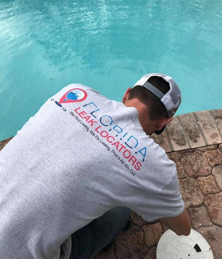 a man wearing a florida leak locators shirt is kneeling next to a pool