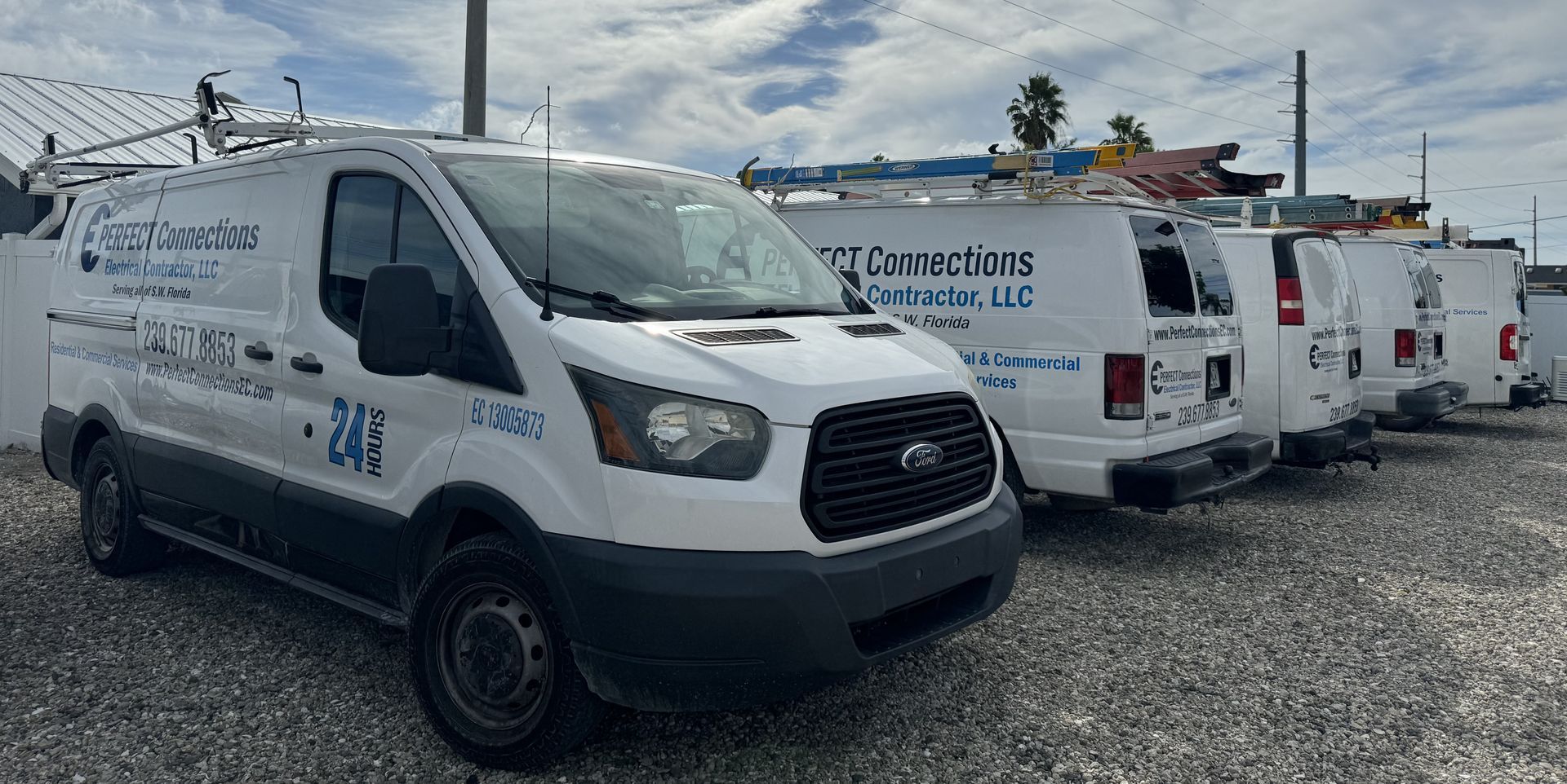 A row of white vans parked in a gravel lot.