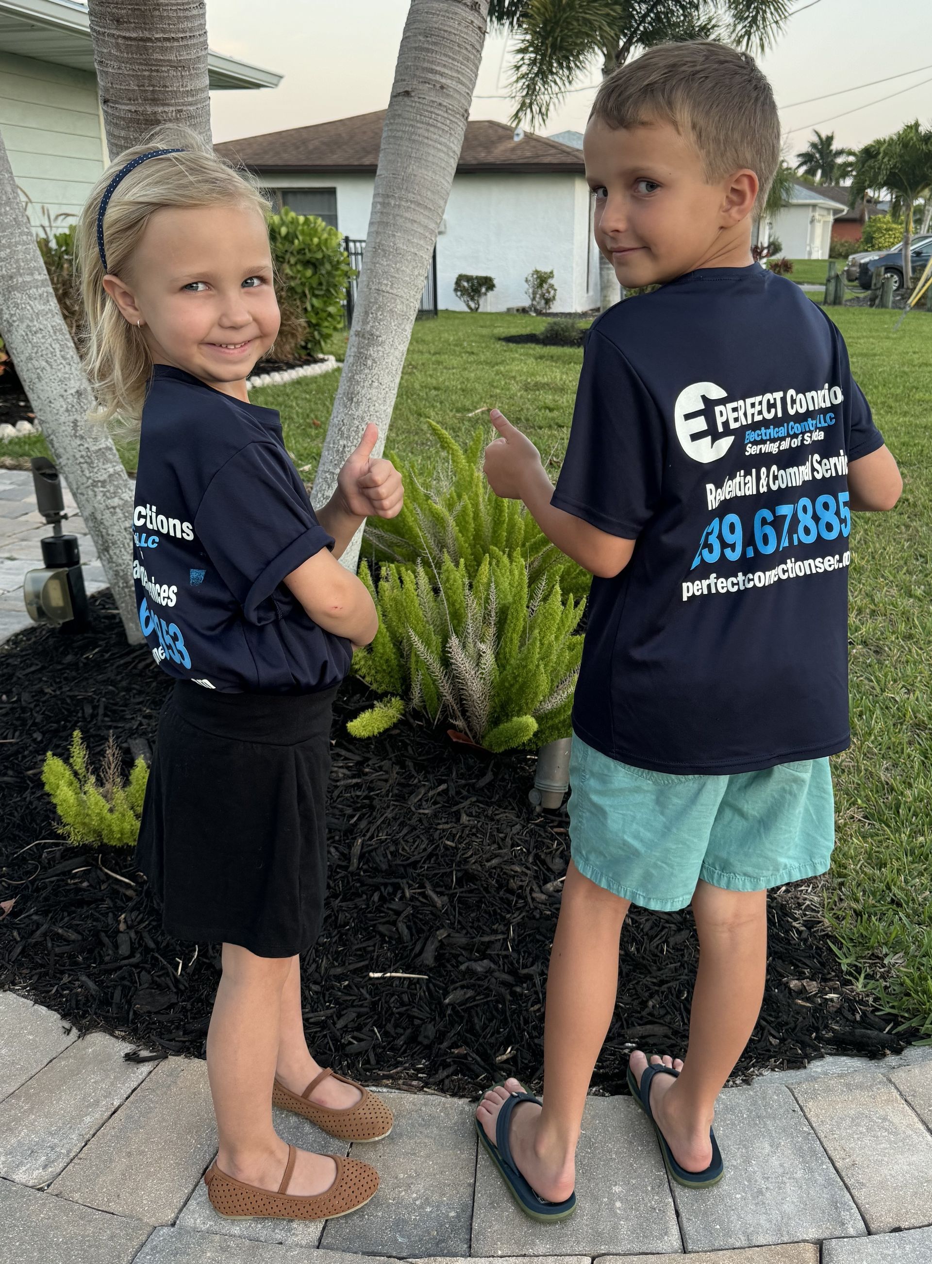 A boy and a girl are standing next to each other in front of a house.