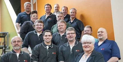 Group of people posing on indoor stairs, smiling and wearing dark jackets and shirts.