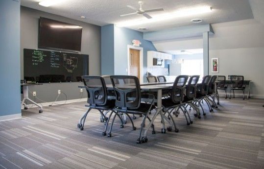 Modern conference room with long table, black chairs, wall-mounted TV, and whiteboard on blue-gray walls