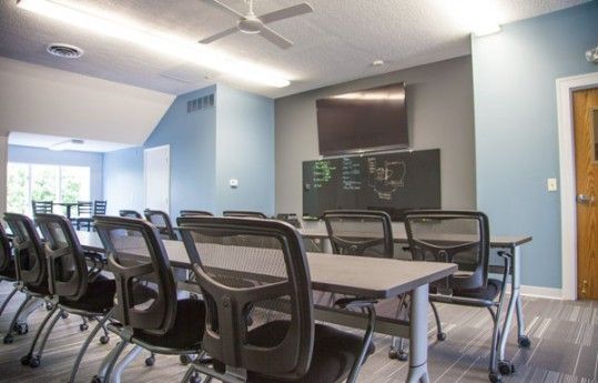 Conference room with long table, black mesh chairs, wall-mounted TV, and large windows.