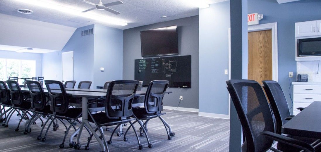 Conference room with black chairs around a long table, wall-mounted TV, and blue walls