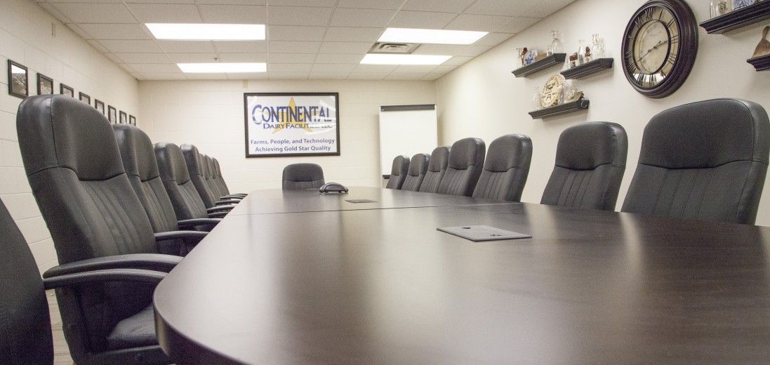 Empty conference room with a long table, black chairs, wall clock, and TV screen