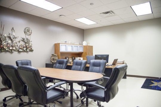 Conference room with oval table, black chairs, and wood cabinet under bright ceiling lights