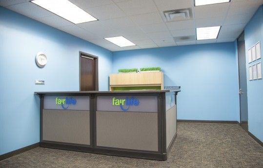Blue office reception area with a front desk, wall clock, door, and fluorescent ceiling lights.