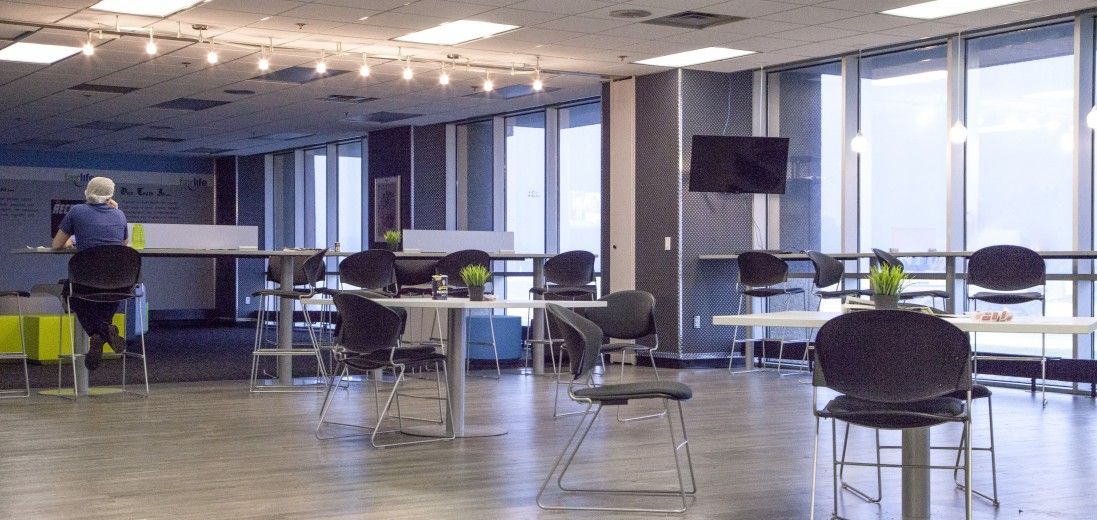 Empty modern office lounge with chairs, tables, and large windows, a person cleaning near the left side