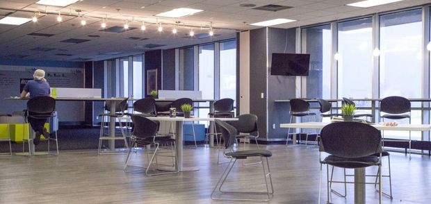Bright modern office lounge with tables, stools, and a person working near the windows