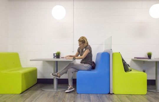 Woman seated at a table in a modern lounge with bright green and blue chairs
