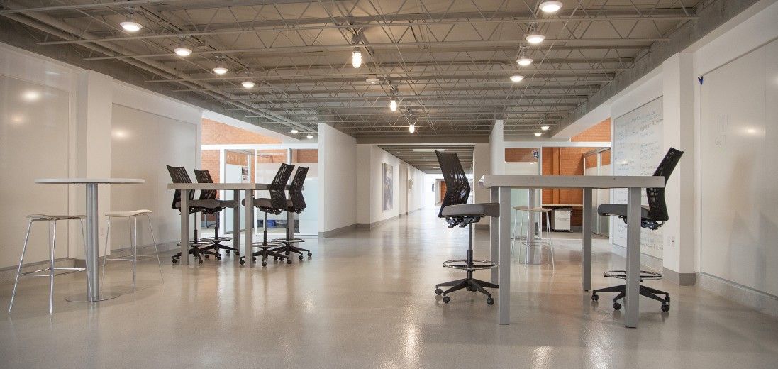 Bright open office with standing desks, stools, and chairs under exposed ceiling lights