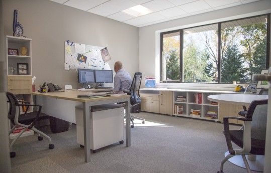 Bright home office with a person at a desk, whiteboard, and large window overlooking trees
