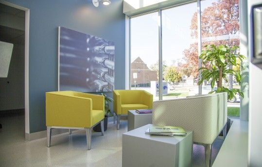 Modern waiting room with yellow and white chairs, a small table, and large windows looking outside