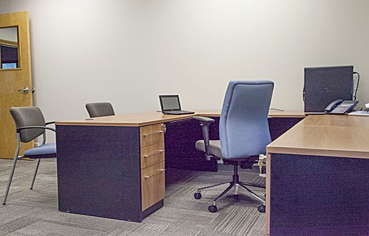 Empty office with desks, blue chairs, a laptop, and a carpeted floor