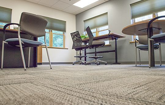 Empty office conference room with chairs and tables, beige carpet, and windows with green blinds