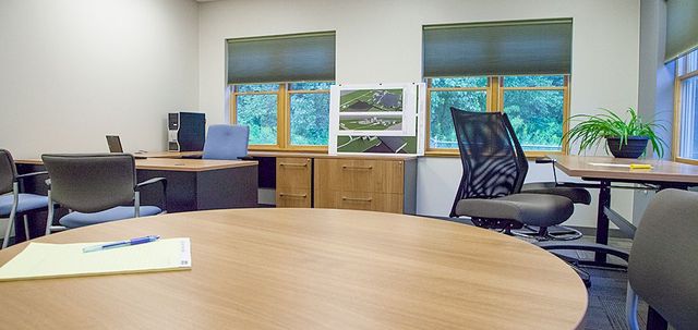 Empty office with desks, chairs, computers, and windows showing trees outside