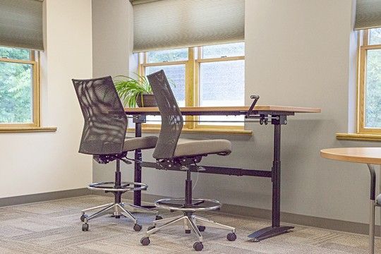 Two office chairs beside a standing desk in a bright room with windows