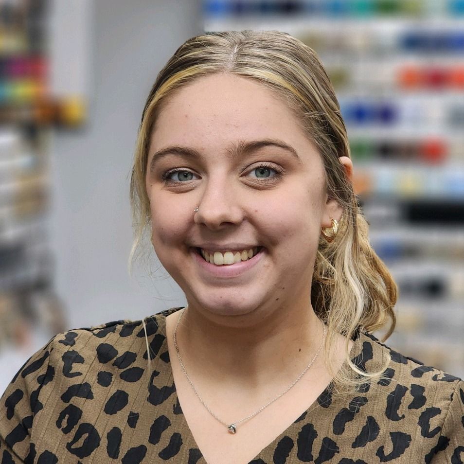 Smiling woman with blonde hair in a leopard-print top, standing in a blurred store aisle.